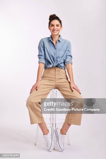 smiling young brunette woman sitting on a stool on gray - part of a series stock pictures, royalty-free photos & images