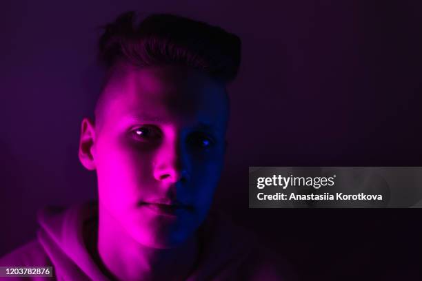 Young guy in a neon light. A teenager in a pink hoodie in trendy lighting of pink, purple and blue