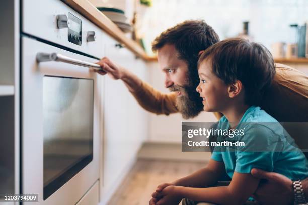 padre e hijo cocinando la cena en casa - horno fotografías e imágenes de stock