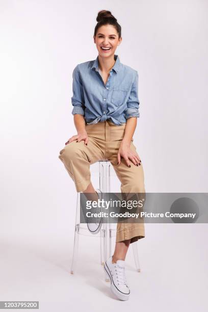 young brunette woman laughing while sitting against a gray background - sitting imagens e fotografias de stock