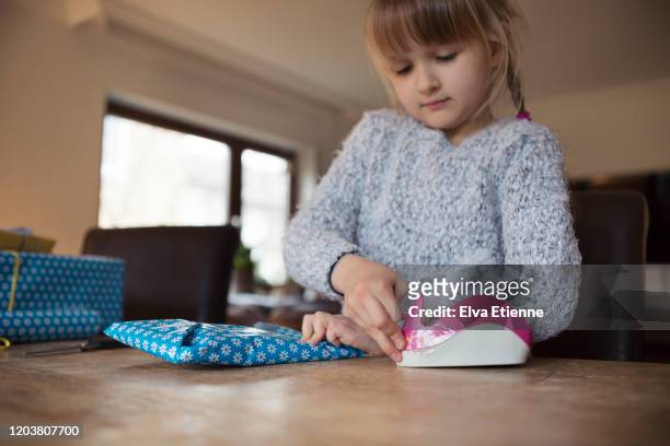 a child using adhesive tape to secure blue wrapping paper around a gift - tape dispenser stock pictures, royalty-free photos & images