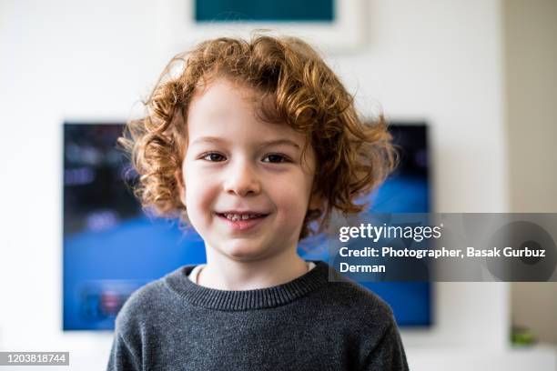 a child standing in front of tv, looking directly to the camera, smiling - boy curly blonde stock pictures, royalty-free photos & images