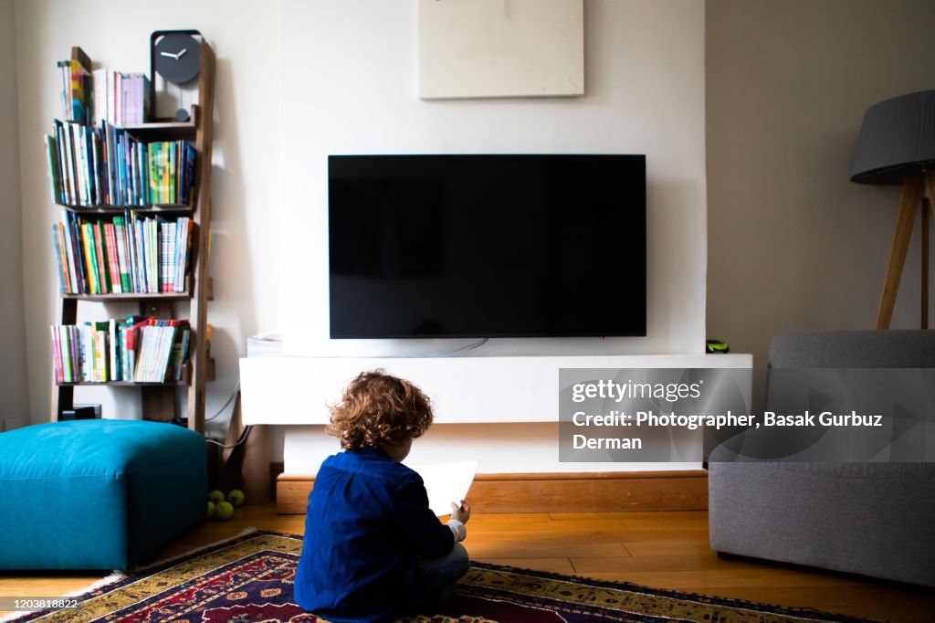 Rear view of a kid sitting in front of tv and reading a book