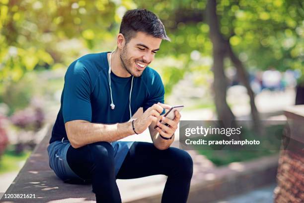 young man is resting and texting in the park after run - young men running stock pictures, royalty-free photos & images