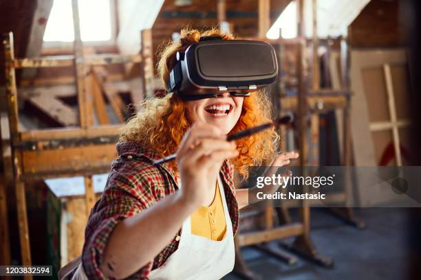 young redhead woman with vr glasses holding paintbrush painting in virtual reality - classroom wide angle stock pictures, royalty-free photos & images