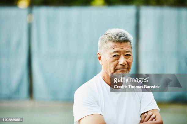 portrait of senior man on tennis court before match - irréductibilité photos et images de collection