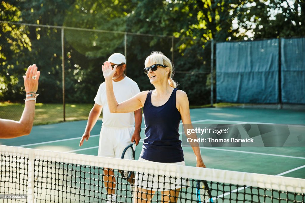 Senior female tennis player high fiving opponent at net after mixed doubles tennis match