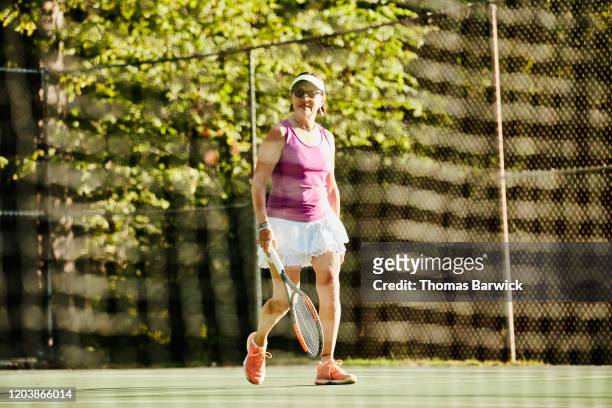 Senior woman walking on to tennis court for early morning match