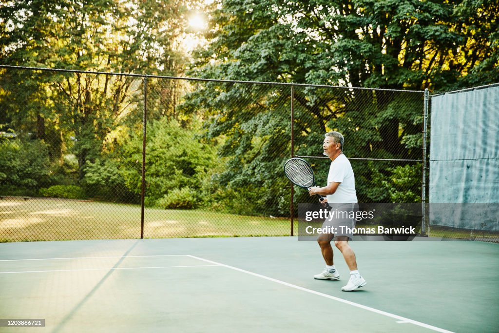 Senior man playing tennis during early morning match