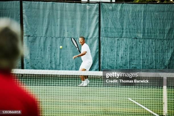 senior man preparing to return shot during early morning tennis match - asian games day 2 stock-fotos und bilder