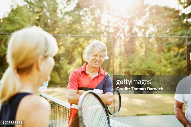 Laughing senior friends in discussion during early morning tennis match