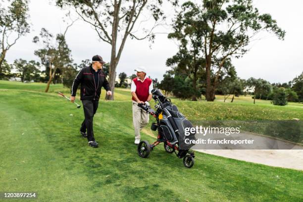 uomo anziano sorridente che spinge le sue mazze su un campo da golf - golf australia foto e immagini stock