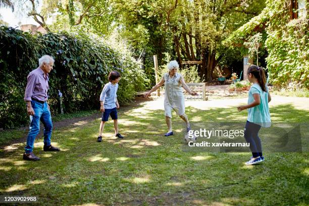 aktive seniorenfußballer kicken ball mit enkelkindern - backyard football stock-fotos und bilder