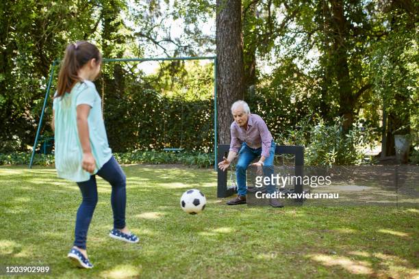 active senior footballer playing with grandchild in backyard - senior kicking stock pictures, royalty-free photos & images