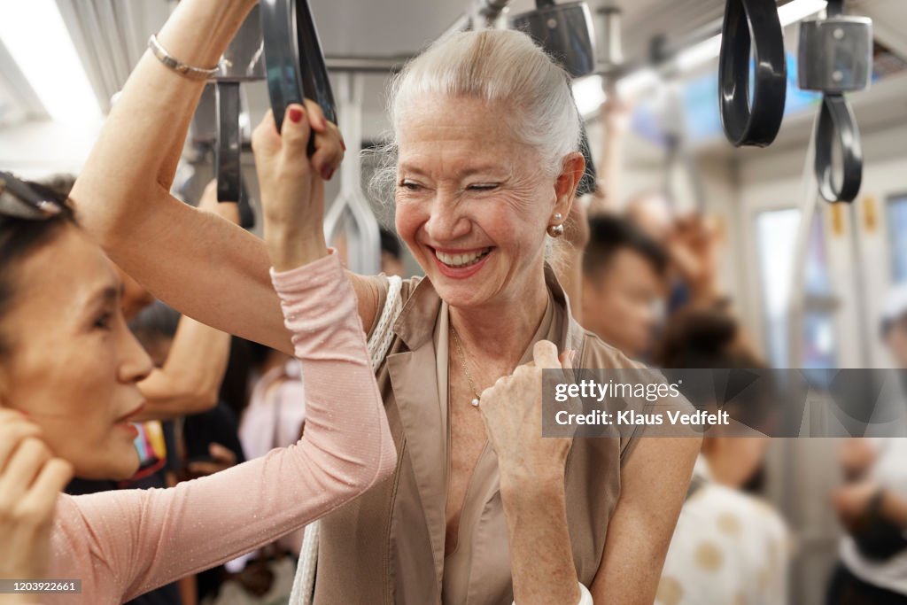 Happy senior female with friend standing in train