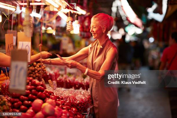 smiling senior woman paying for fruit in market - tourist market stockfoto's en -beelden