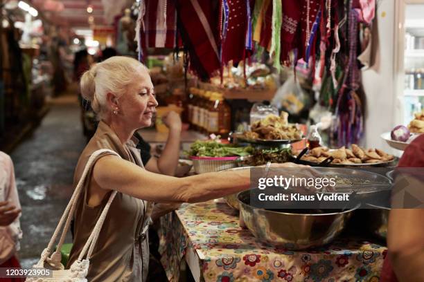 senior woman sitting at fast food stall in market - food stall bildbanksfoton och bilder