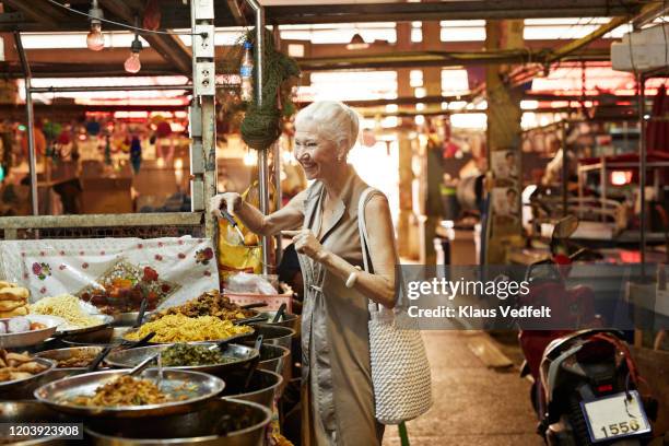 smiling senior woman at fast food stall in market - comida tailandesa fotografías e imágenes de stock