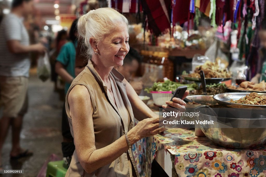 Senior woman using phone at food stall in market