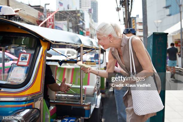 senior woman giving money to driver in city - thailand tourist stock pictures, royalty-free photos & images
