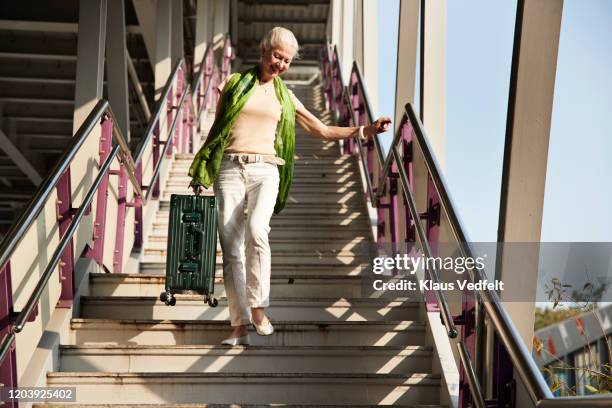 senior woman moving down stairs with luggage - carry on luggage photos et images de collection