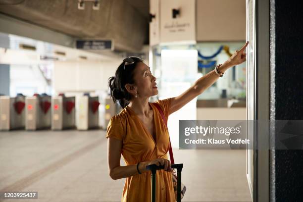 mature woman looking at map on railroad station - departure board front on fotografías e imágenes de stock