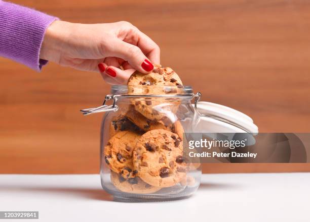 woman's hand taking a chocolate chip cookie - eating cookies foto e immagini stock