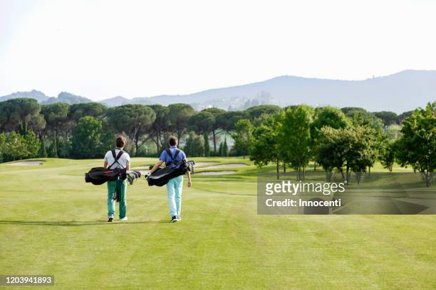 friends carrying golf bag walking on golf course - bolsa de golf fotografías e imágenes de stock