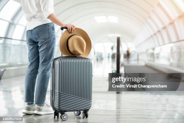 female passenger with her weave hat hipster style and suitcase standing in the terminal - luggage stock-fotos und bilder