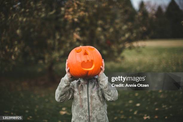 boy holds a jack-o-lantern in front of his face - schnitzen stock-fotos und bilder