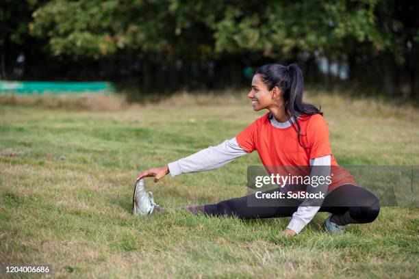profile view of woman stretching on grass before event - stretching hamstring stock pictures, royalty-free photos & images