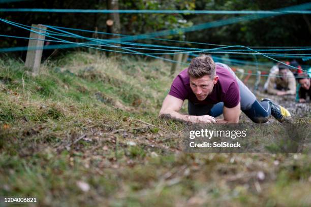 hombre luchando en las manos y las rodillas en la carrera de obstáculos al aire libre - campamento de instrucción militar fotografías e imágenes de stock