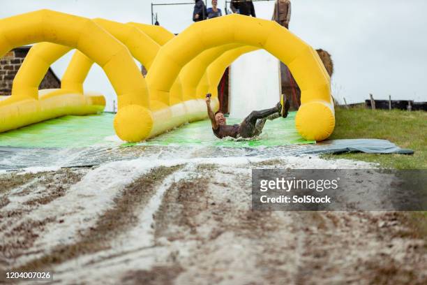 man having fun on muddy inflatable slip and slide - mudslides stock pictures, royalty-free photos & images
