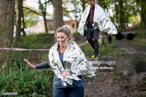 woman wearing foil blanket running along woodland path - people covered in mud stock pictures, royalty-free photos & images