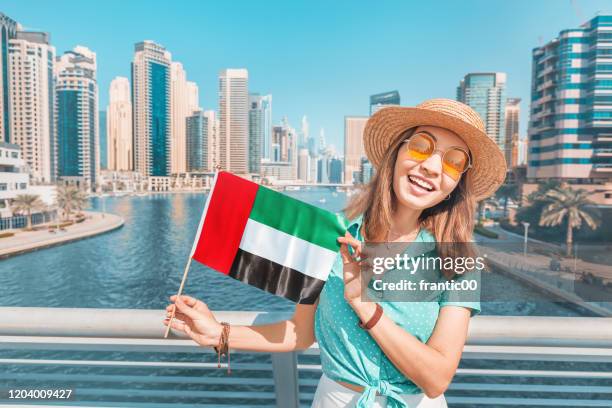 Woman holding national flag of United Arab Emirates, while standing in Marina district of Dubai