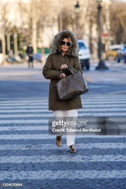 Guest wears sunglasses, a khaki padded coat with a fur-trimmed hood, white pants, lustrous bronze-tone boots, a large brown croc-effect tote bag,...