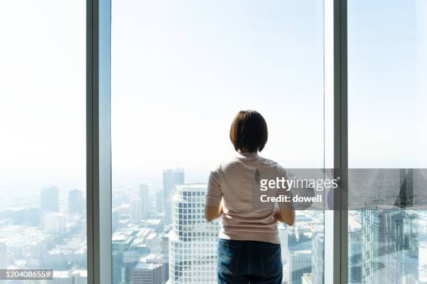 woman holding smart phone and standing in front of window - smart communicate elevation view stockfoto's en -beelden