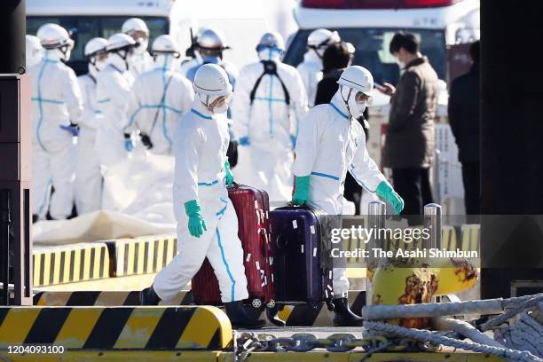 Health officials wearing protective gears carry the suitcases believed to belong to patients who confirmed positive for new coronavirus as they are...