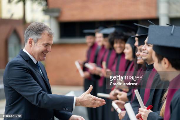 happy headmaster giving a handshake to students on their graduation day - dean stock pictures, royalty-free photos & images