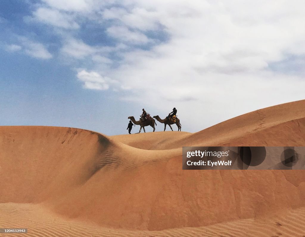 Two people riding camels on dunes in Essaouira, Morocco