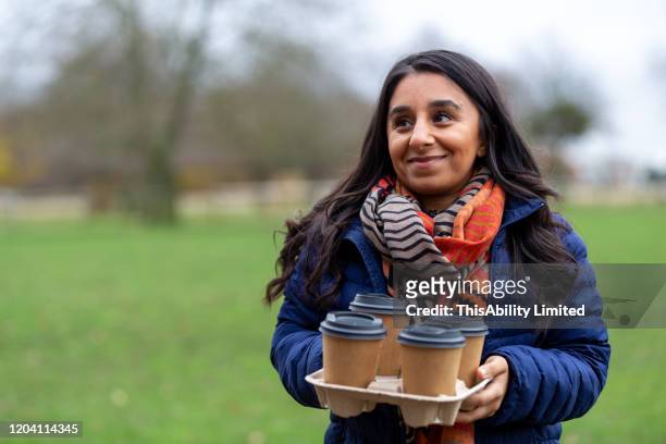 smiling woman with disposable coffee cups standing in park - disabilitycollection stock pictures, royalty-free photos & images