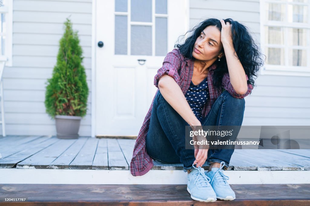 Traurige mittlere erwachsene Frau sitzt auf einer Treppe vor ihrem Haus
