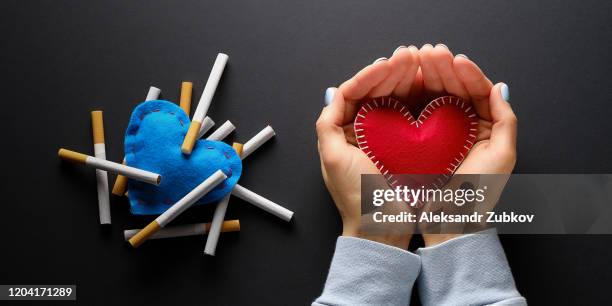 red heart or valentine in the hands of a girl, on a black background. nearby, cigarettes lie on a blue decorative heart. smoking destroys health. social problem. - smoke heart stock pictures, royalty-free photos & images