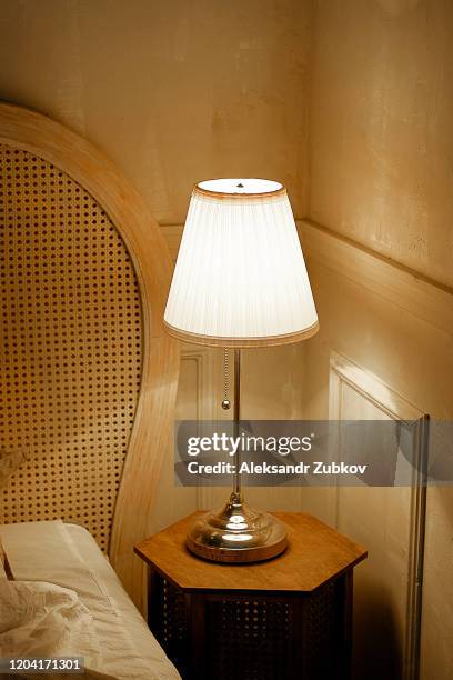 an old-fashioned classic table lamp is turned on in a dark room. - bedside table lamp stock pictures, royalty-free photos & images