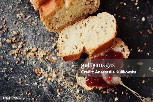 Baton with raspberry jam. Fresh pastries with flax seeds. Dark background, view from above. Raspberry jam on a piece of bread and a silver vintage spoon. Baton with raspberry jam. Fresh pastries with flax seeds. Dark background, view from above. Raspberry jam on a piece of bread and a silver vintage spoon.