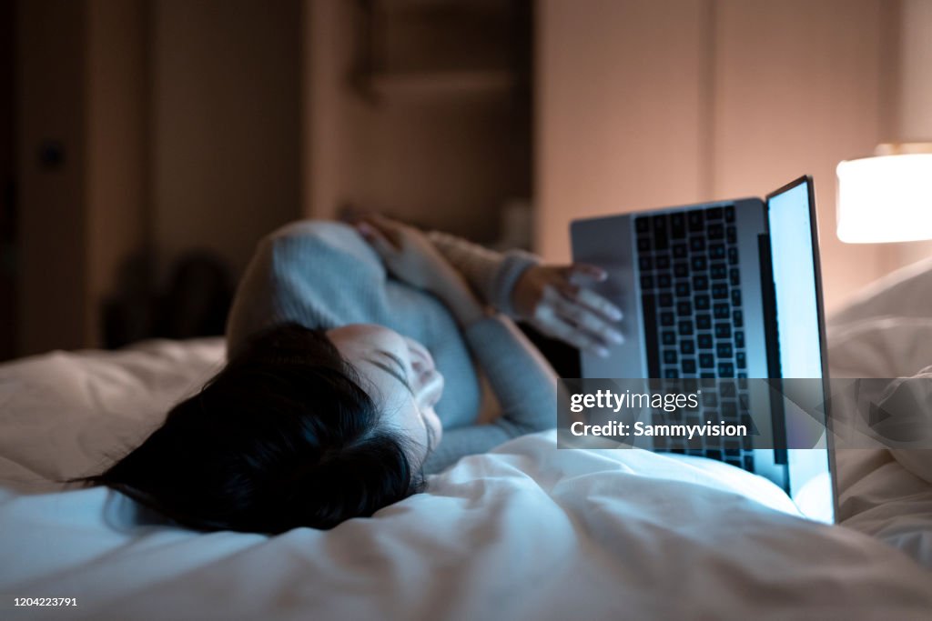 Asian woman working with laptop on the bed