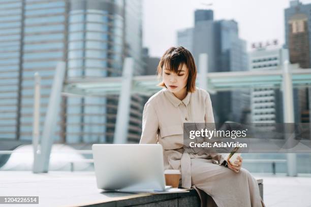 young urban asian businesswoman working on laptop while having lunch on a urban balcony - business lunch outside stock pictures, royalty-free photos & images