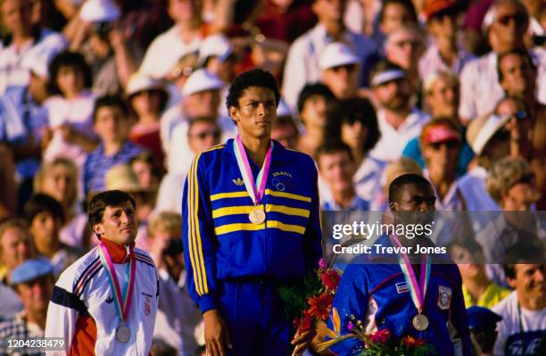 Joaquim Cruz of Brazil stands on the podium with his gold medal alongside silver medallist Sebastian Coe and bronze medallist Earl Jones after...