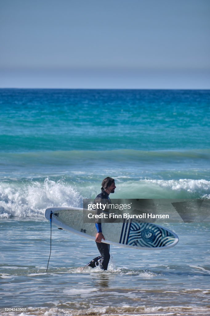 Male surver walking in the water a the beach carrying a surfboard