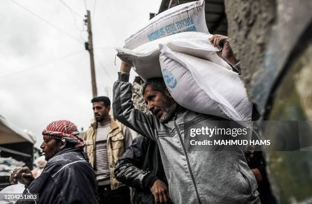 Palestinian carries sacks of flour as people receive food aid from a United Nations Relief and Works Agency distribution centre at al-Shati refugee...